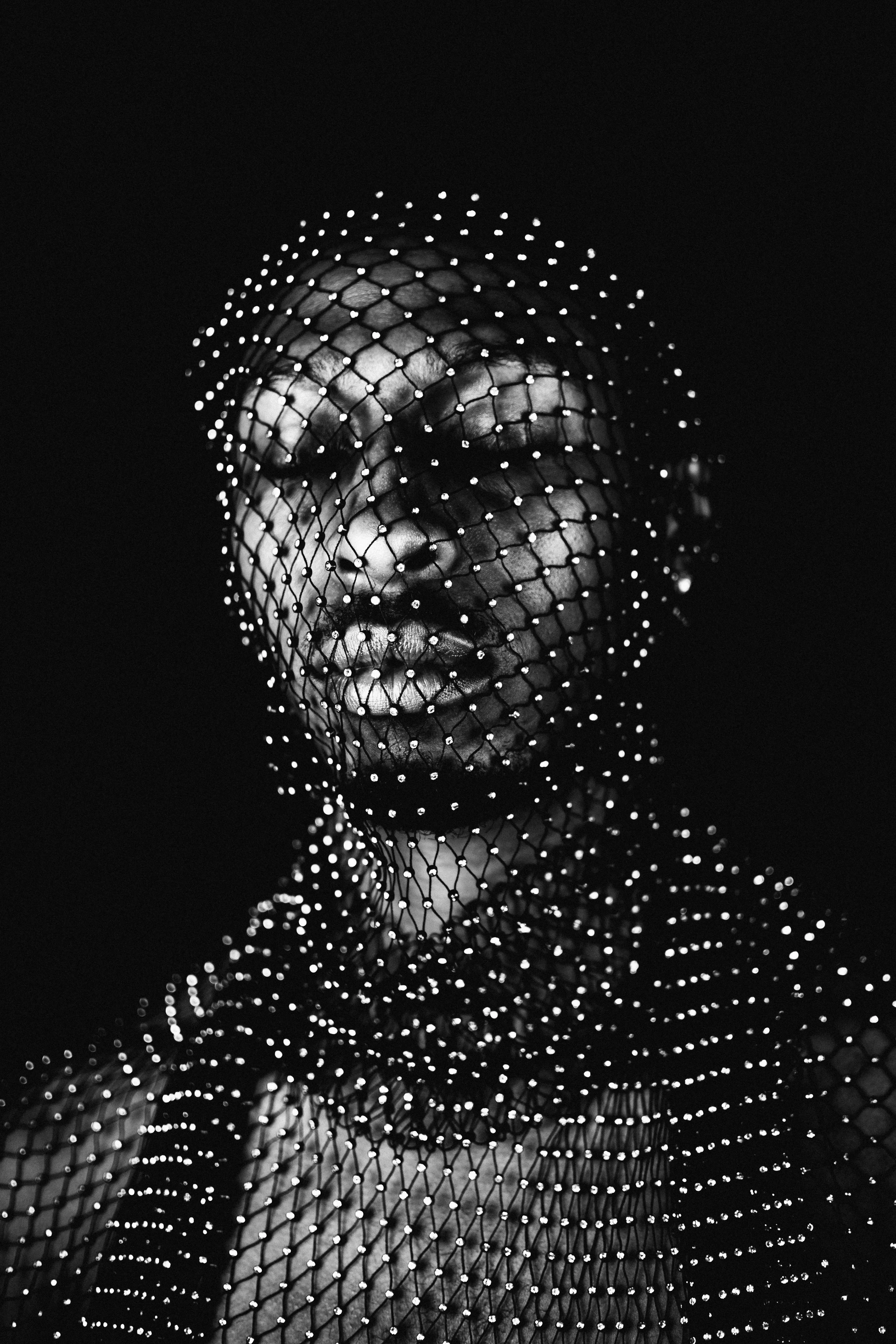 Black and white photograph by Agostina Cerullo. A man draped in a mesh sequined veil is depicted in a close-up shot