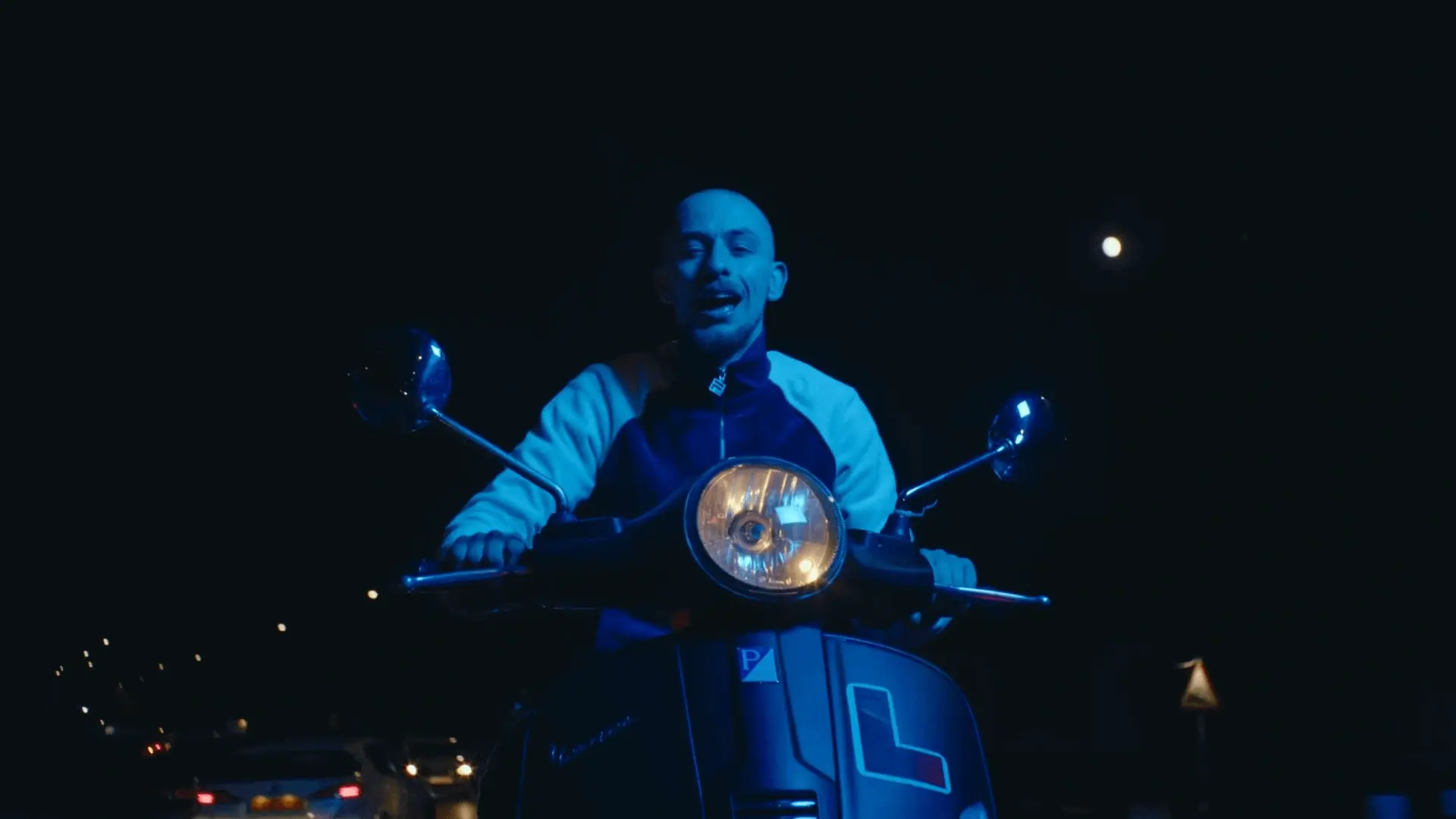 Screenshot from the 'Round Here' music video by Finn Foxell with cinematography by Chaimaa Ormazabal (Chaimuki). Image shows Finn riding a motorbike in the night streets drenched in blue lighting.