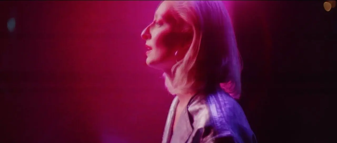 A neon-soaked, pinkish-purple-toned scene from the music video 'UNSUNG', directed by Martyn Thomas, featuring a singer in profile under strobe lighting.