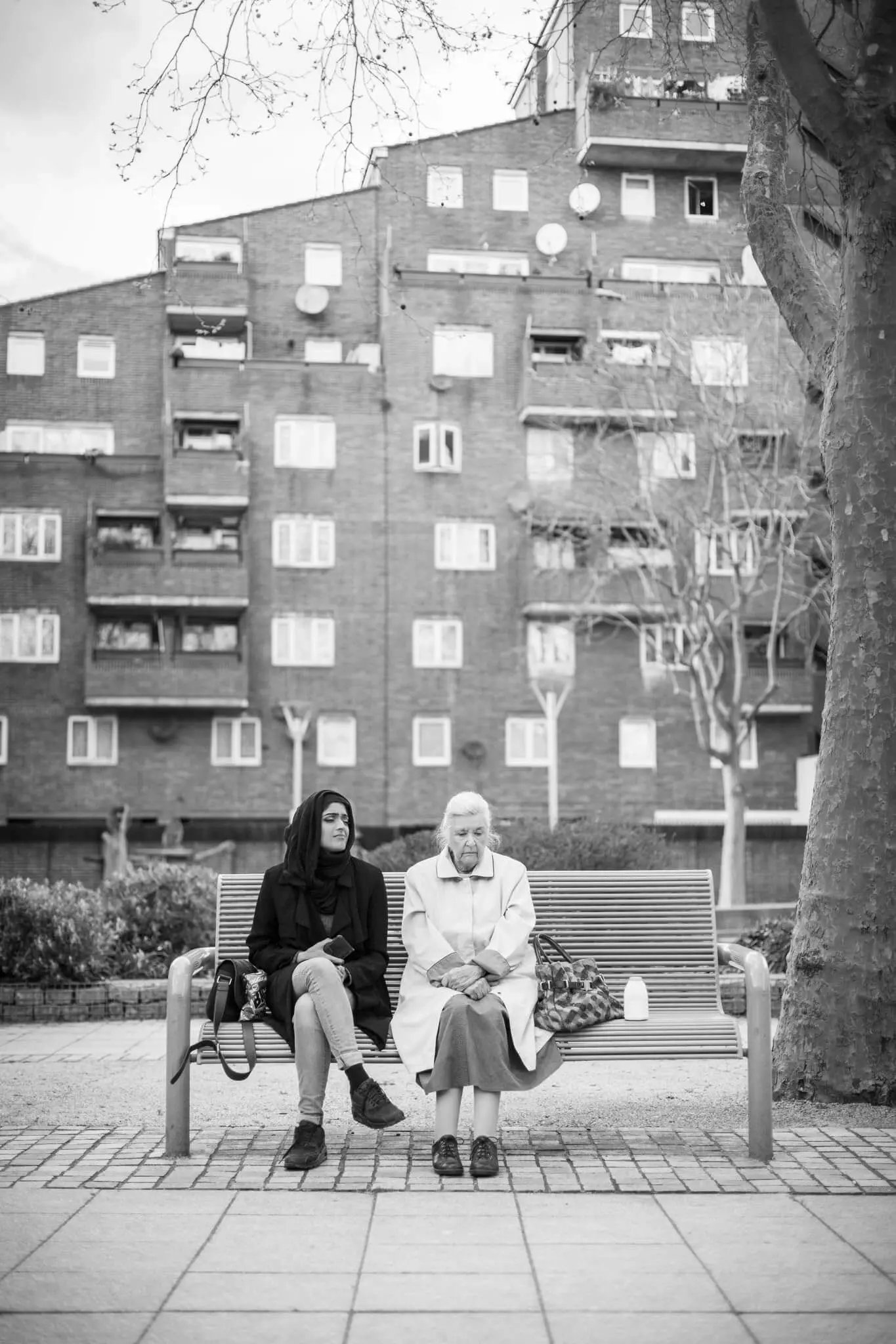 A poster image from the short film 'Mrs Taylor' directed by Martyn Thomas. The image depicts a lady and an elderly woman sitting on a bench in a residential area, captured in black and white.