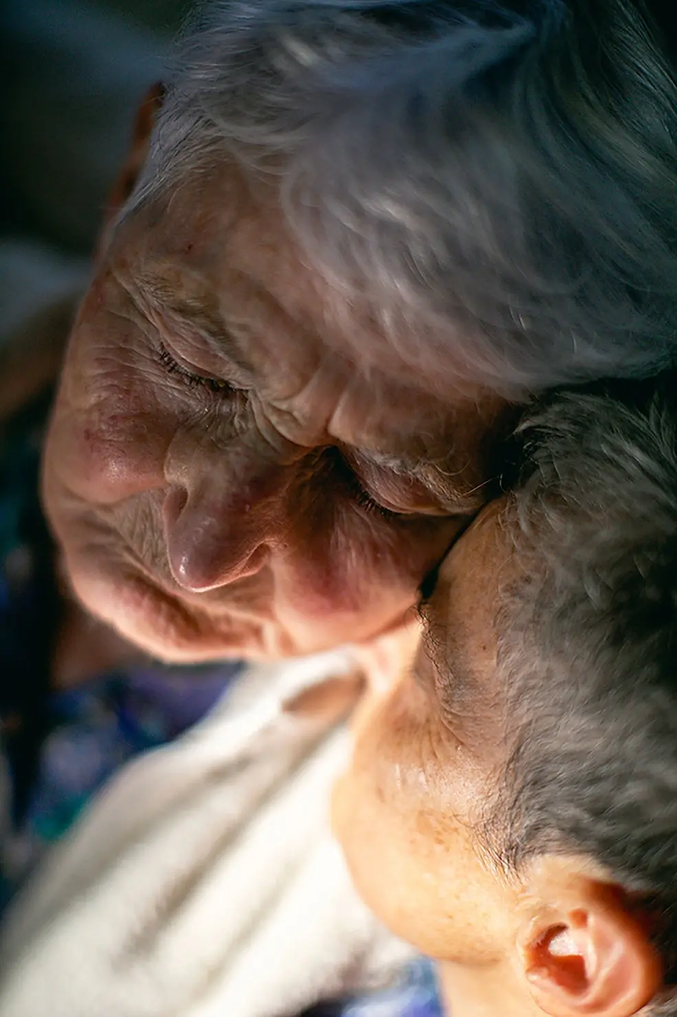 Close-up portrait photograph of two elderly women embracing each other warmly, expressing love and companionship.