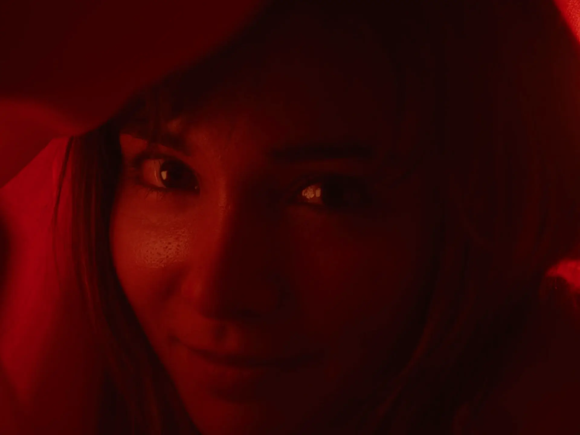 Neon red soaked screenshot from the film 'Malibu' directed by John C Stallings with cinematography by Chaimaa Ormazabal, depicting a close-up of an actress staring deeply into the camera with a subtle smile on her face.