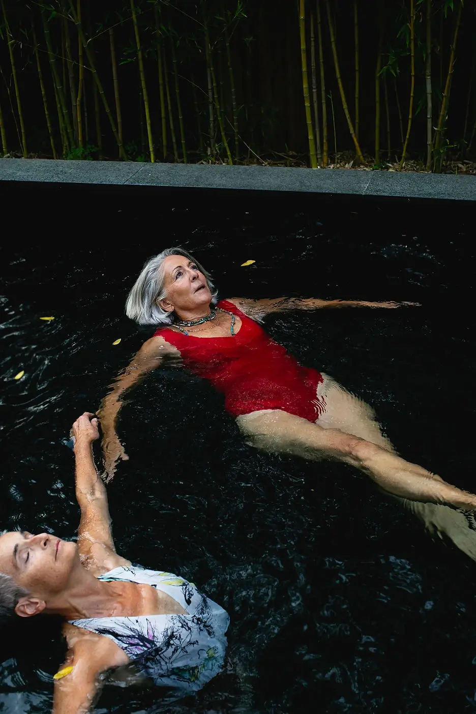 Two elderly women floating peacefully in a pool, gazing up at the sky, enjoying a serene moment of relaxation.