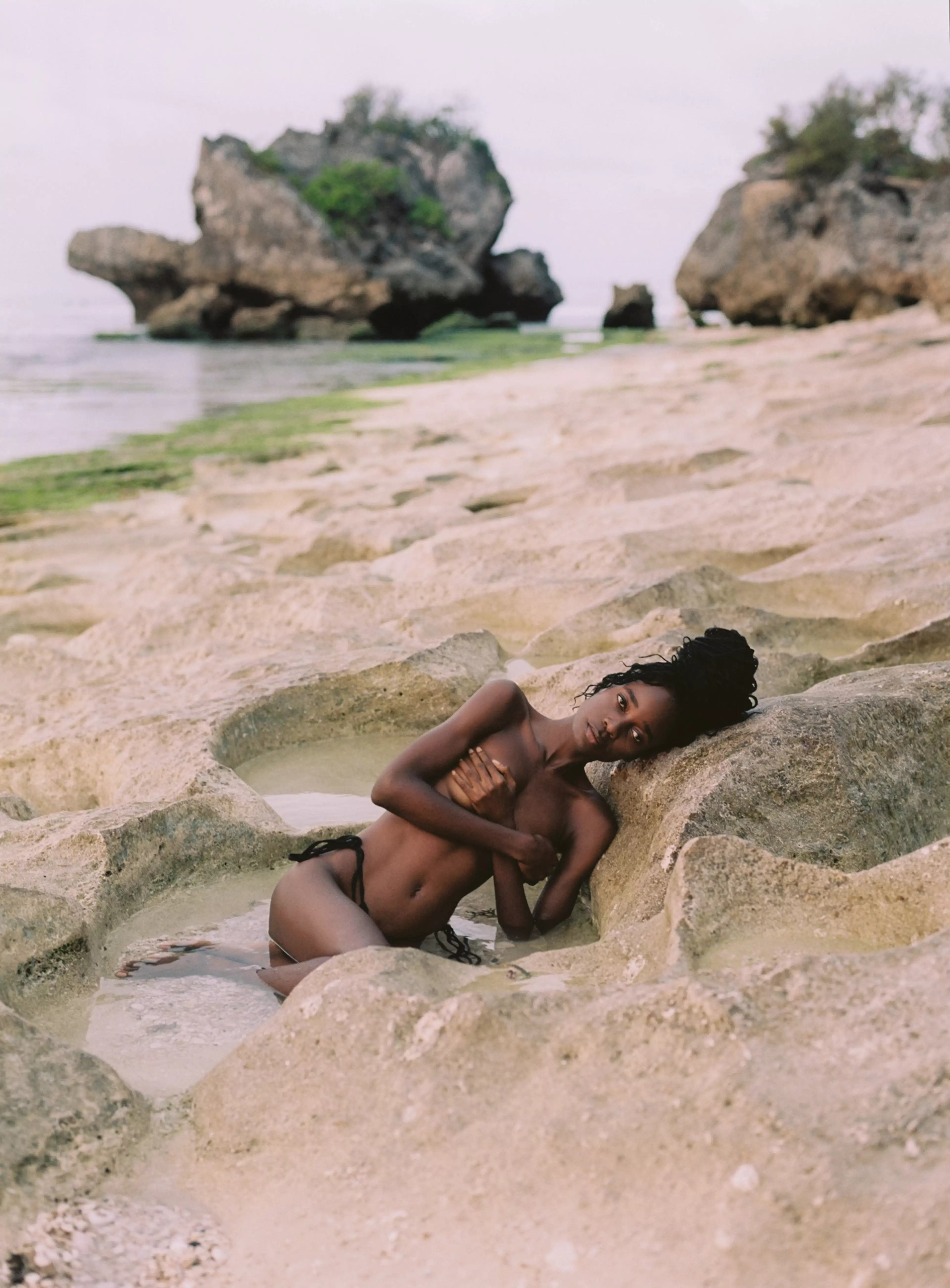 Photograph by Agnes Wonke-Toth. Model Irene reclines in a sandy crevasse on the beach, her gaze fixed upon the camera.