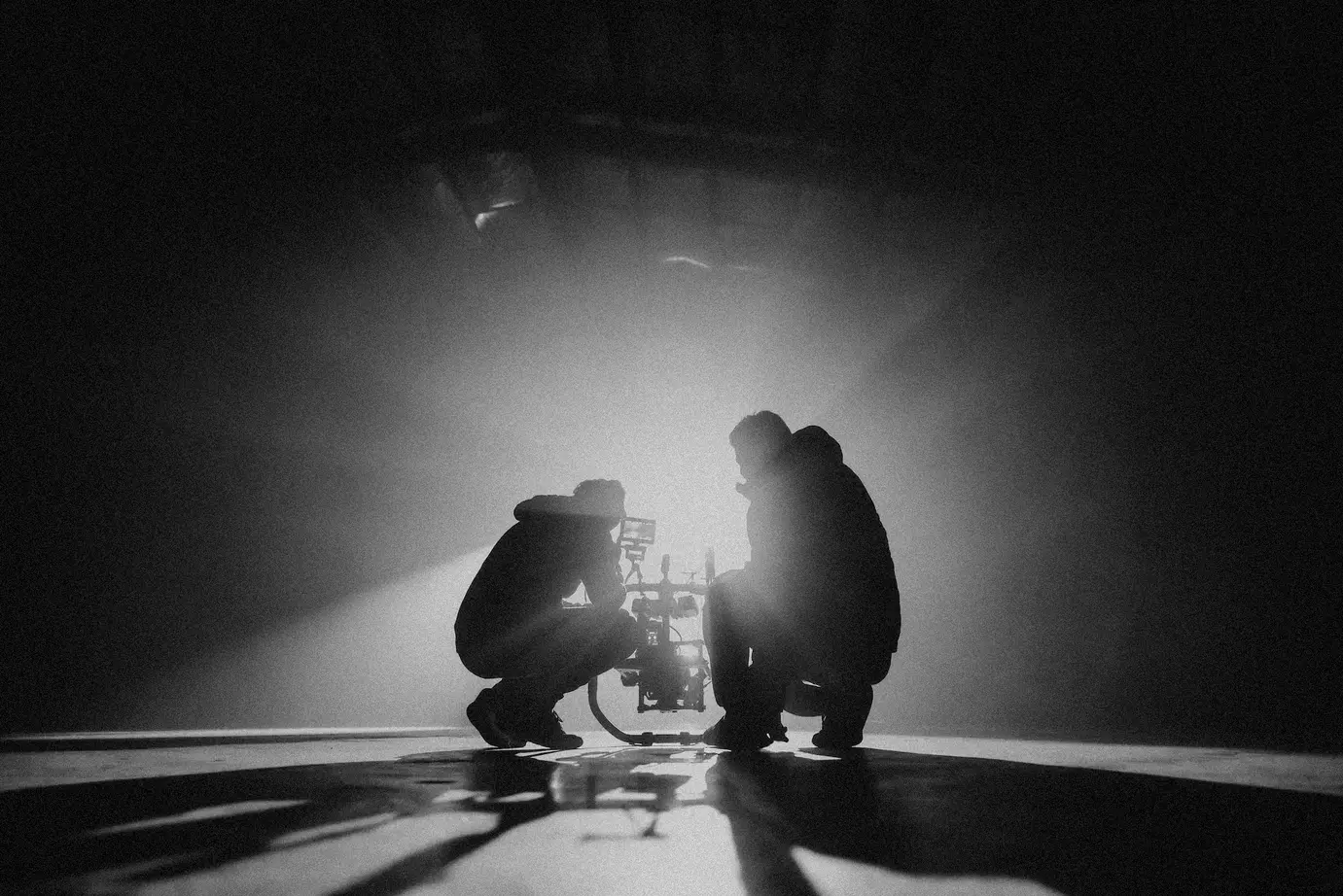 grayscale photography of two crouching men. Director and Producer line up camera shot before action is called. Image by Natalie Parham on Unsplash